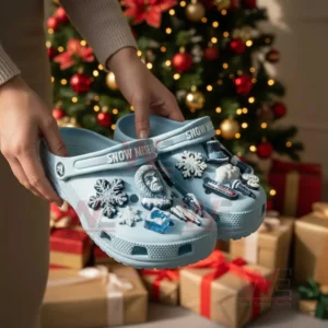 Winter themed light blue clogs with snow charms held by hands in a festive Christmas setting with tree lights and gift boxes!