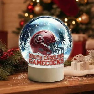 A snow globe containing a South Carolina Gamecocks football helmet surrounded by snowy trees on a holiday decorated table.