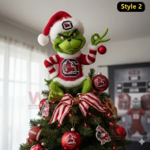A green character in festive clothing sits on the top of a Christmas tree holding a red ornament.