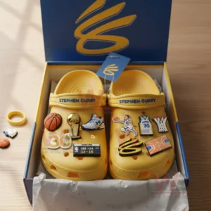 A pair of yellow basketball themed clogs shown in an open box featuring multiple decorative charms inspired by the sport and a famous player!