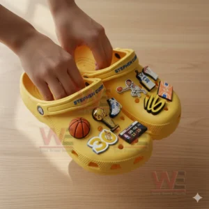 A close view of yellow sporty clogs adorned with various basketball themed charms touched lightly by hands!