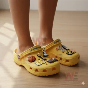 Feet wearing yellow decorative clogs adorned with basketball themed charms in a bright indoor setting!