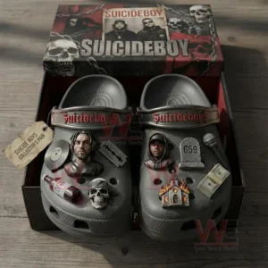 Open shoebox showing gray clogs with red strap lettering and dark themed charms including skull microphone razor blade bottle tombstone marked G59 burning building and money.