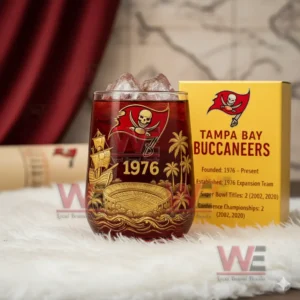 A red Buccaneers themed ice filled glass with gold detailing next to a yellow team box on a white furry surface!