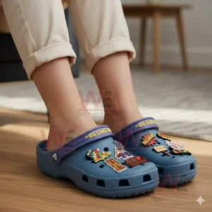 Feet wearing blue decorative clogs adorned with sitcom inspired charms shown in a cozy indoor setting!