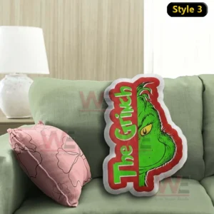 Stylized Grinch face pillow with text design resting on a green sofa next to a pink cushion!