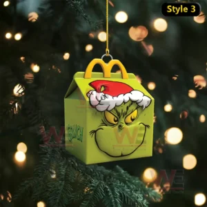 A green McDonalds themed box ornament with a grinning face hangs in front of a softly lit Christmas tree!