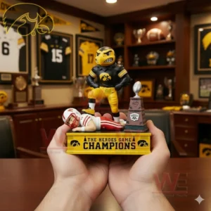 Hands holding an Iowa Hawkeyes mascot figure on a The Heroes Game Champions base with a defeated opponent player and a small trophy display in the background.