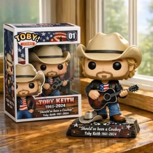 A vinyl style country musician figure with a cowboy hat and guitar standing on a base beside its display box on a wooden table by a window!