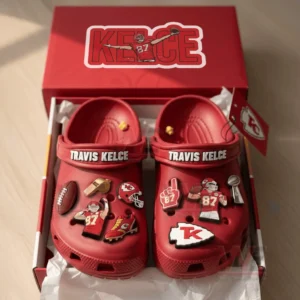 A boxed pair of red Travis Kelce themed clogs decorated with football charms displayed neatly inside packaging!