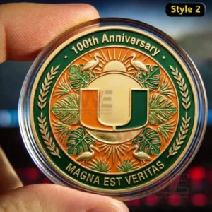 Fingers holding a University of Miami 100th Anniversary coin with the green and orange U logo sun rays tropical leaves and the text Magna Est Veritas inside a clear case.