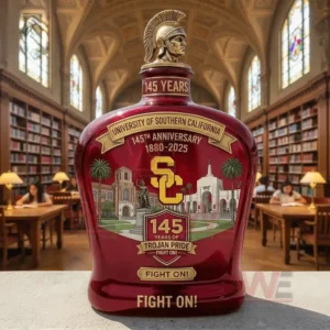 USC commemorative whiskey bottle in deep red with Trojan helmet topper one hundred forty five years text eighteen eighty to two thousand twenty five anniversary label USC initials campus landmark illustrations and Fight On slogan in a library setting!