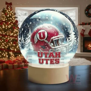 A snow globe displaying a red Utah Utes football helmet set in a snowy forest scene placed in a warmly lit holiday decorated living room.