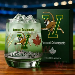 Green Vermont Catamounts whiskey glass with ice mountain graphics claw marks and maple leaf placed next to a branded green box in a stadium setting!