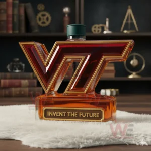 Virginia Tech Hokies Invent The Future Custom Whiskey Bottle 7 A VT shaped amber bottle with a green cap placed on a white mat in a room with books and mechanical decor pieces!