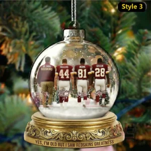 A glass holiday ornament featuring a coach and three Washington football figures seen from behind walking across a snowy scene with festive lights in the background.