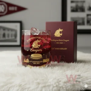 A red drink with ice rests in a gold printed anniversary glass on a white fur surface with a matching box in the background.