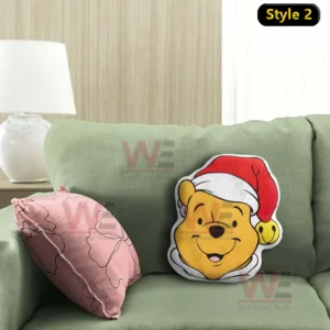 Yellow bear face Christmas pillow with a red Santa hat displayed on a green sofa with a soft pink cushion nearby!
