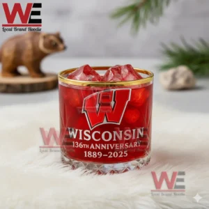 A red Wisconsin anniversary glass with ice placed on a white furry mat with a wooden bear and greenery in the background!