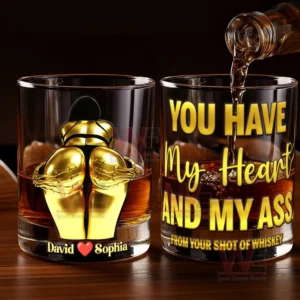 Two stylish whiskey glasses with a golden hugging couple design and dark whiskey on a wooden table under warm light!
