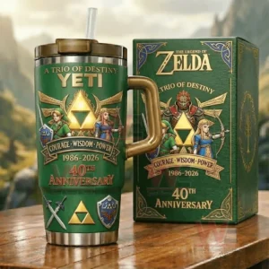 A green The Legend of Zelda collector tumbler with a gold handle and straw featuring Link Zelda Ganondorf and a Triforce next to a matching anniversary box on a wooden table!