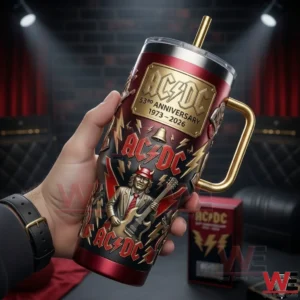 Hand holding a red black and gold ACDC themed metal tumbler with guitarist artwork lightning symbols gold handle and straw against a dark stage background!