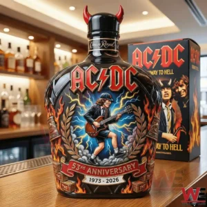 A decorated ACDC anniversary whiskey bottle with vivid artwork flames lightning and a guitarist illustration placed on a wooden bar surface with a themed box in the background!