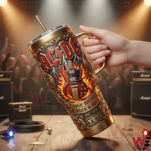 A hand holding an AC DC themed insulated tumbler in front of a concert stage with amplifiers lights and a cheering crowd!