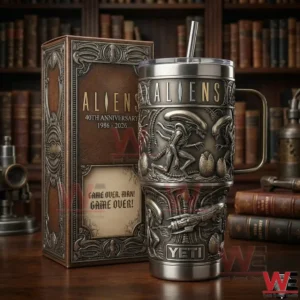 An Aliens insulated tumbler with detailed alien artwork shown next to its anniversary box on a wooden table with books behind!