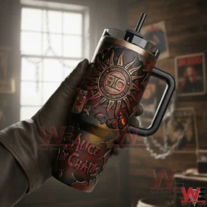 Gloved hand holding an Alice In Chains insulated tumbler with handle straw and dark vintage artwork with a softly blurred indoor background.