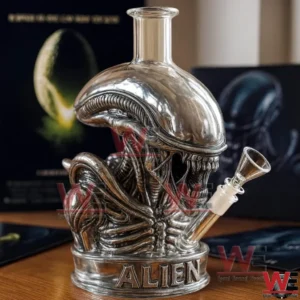 Silver alien xenomorph shaped glass bong with clear neck and angled bowl displayed on a wooden table with movie posters in the background!