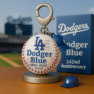 Dodgers baseball keychain with LA logo Dodger Blue text 1883 to 2025 142nd and a blue anniversary box on a table in a stadium background.
