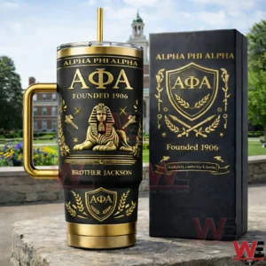 Black and gold Alpha Phi Alpha insulated tumbler with handle and straw next to an elegant matching box displayed outdoors on a stone surface with a historic academic building in the background!