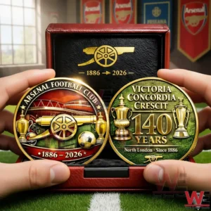 Hands holding an Arsenal 140th anniversary commemorative coin set in a red display case with two gold coins showing Arsenal cannon design 1886 to 2026 stadium artwork trophies and Victoria Concordia Crescit 140 years text