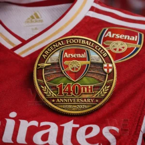 Arsenal 140th anniversary coin with club crest stadium design and 1886 2026 text placed on a red jersey with Arsenal badge