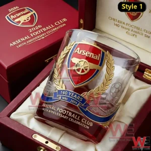 A close up view of an Arsenal anniversary whiskey glass resting inside a red wooden gift box with gold accents and official club emblem visible on the glass and box interior!
