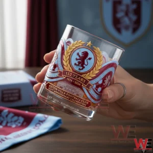 A close view of a hand holding an Aston Villa anniversary whisky glass with intricate crest artwork and one hundred fifty two year celebration theme!