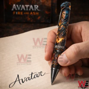Hand holding an Avatar Fire And Ash themed pen above a notebook with the word Avatar written on the page and a blurred title sign in the background.
