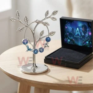Silver adjustable charm bracelet with blue Avatar inspired charms hanging on a leaf jewelry stand next to an open black presentation box on a wooden table.