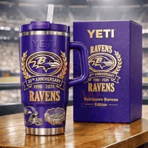 Purple YETI Ravens 30th Anniversary tumbler next to a purple Ravens themed gift box on a table with a blurred stadium behind!