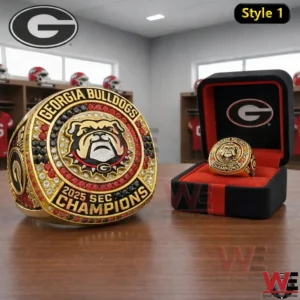 A close view of a Georgia Bulldogs 2025 SEC Champions championship ring with a bulldog logo red black and clear stones on a wooden table with a matching ring box behind it!