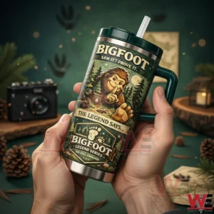 Hands holding a dark green Bigfoot themed insulated tumbler with straw and handle featuring forest artwork and bold Bigfoot text!