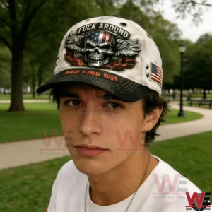 Young man in a park wearing a beige and black baseball cap with a skull wings flames graphic and an American flag patch.