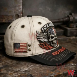 Three quarter side view of a beige and black baseball cap with a skull wings flames graphic plus an American flag patch and metal rivets on the side.