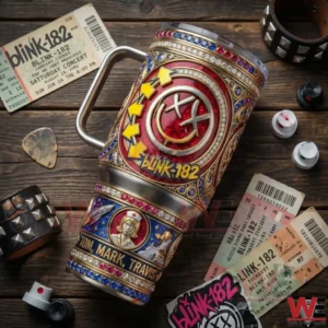 A Blink 182 tumbler with ornate gold details rests on a wooden table with concert tickets and music accessories nearby!