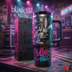 Blink 182 insulated tumbler with handle and straw next to a matching themed box on a wooden table with colorful concert style lighting and music posters in the background.