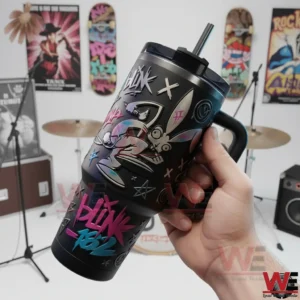 Hand holding a Blink 182 insulated tumbler with handle straw graffiti artwork and bunny character with a blurred drum kit and music posters in the background.