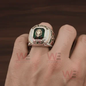Close up of a hand wearing a large Bob Marley One Love themed ring with a green gemstone center lion emblem sparkling stones and engraved text around the face!