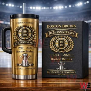 Gold Boston Bruins collector edition tumbler with handle and straw beside a matching anniversary box on a wooden table with a blurred hockey arena background!