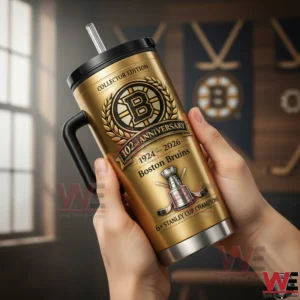 Hands holding a gold Boston Bruins anniversary insulated tumbler with handle and straw with hockey themed wall decor in the background!
